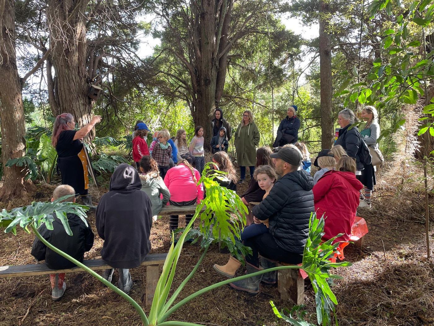 An outdoor lesson under the trees with students and whānau listening