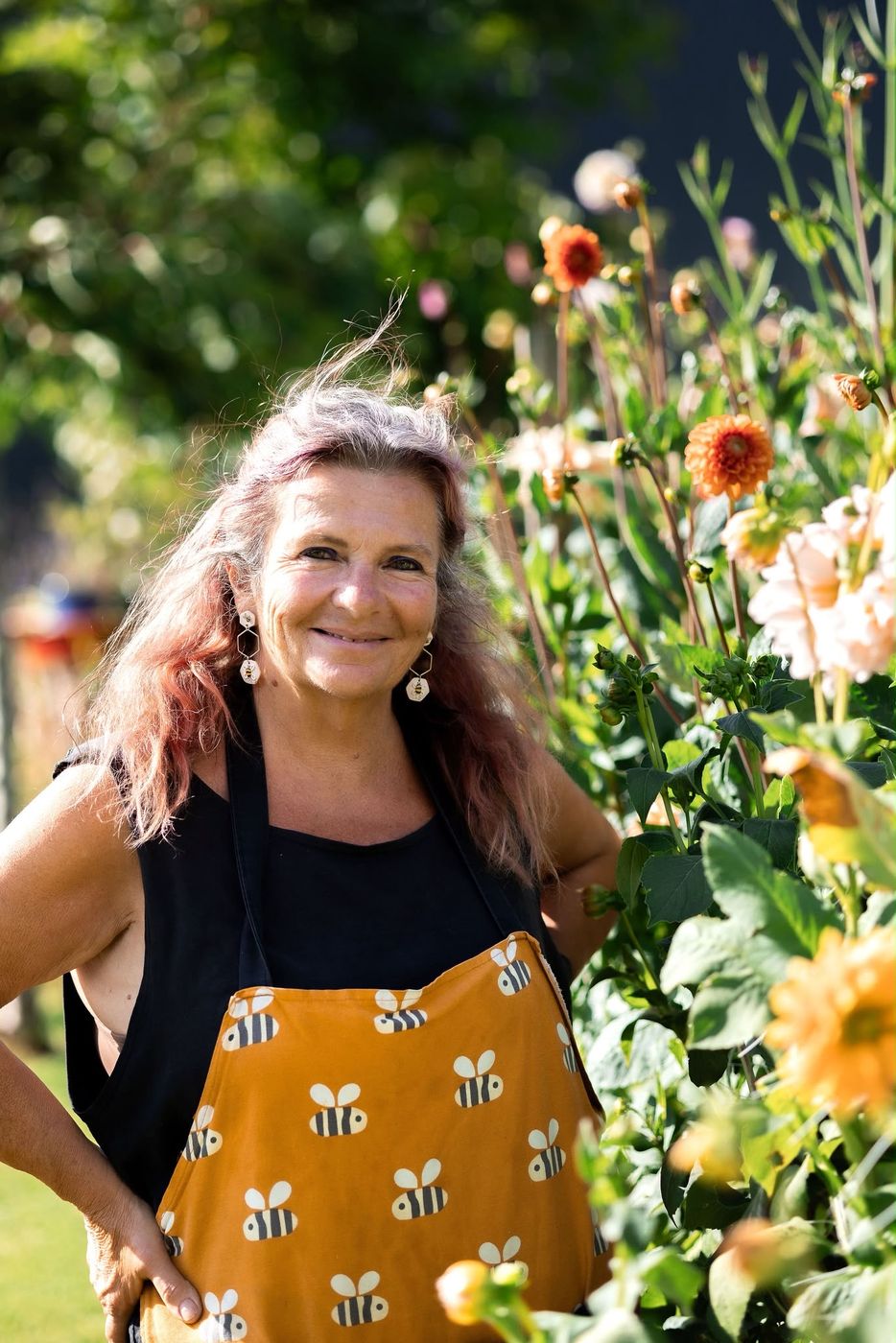 A smiling beekeeper in a bee-print apron among dahlias in the garden