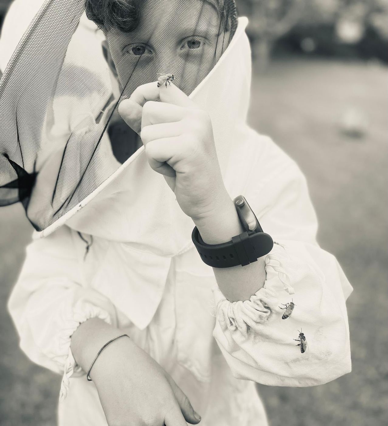 A student in a bee veil looking closely at a bee resting on their finger